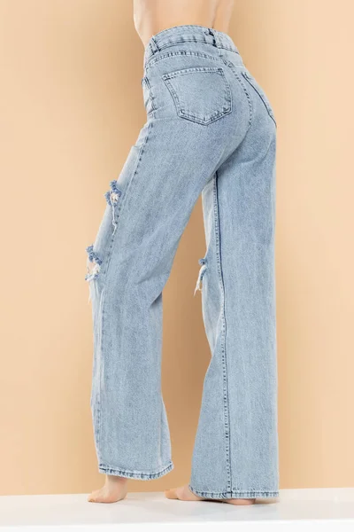 Pernas Uma Mulher Jeans Rasgado Fundo Estúdio Bege Lado Vista — Fotografia de Stock