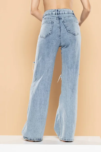 Pernas Uma Mulher Jeans Rasgado Fundo Estúdio Bege Voltar Visão — Fotografia de Stock