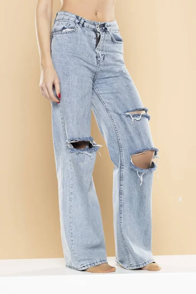 Pernas Uma Mulher Jeans Rasgado Fundo Estúdio Bege — Fotografia de Stock