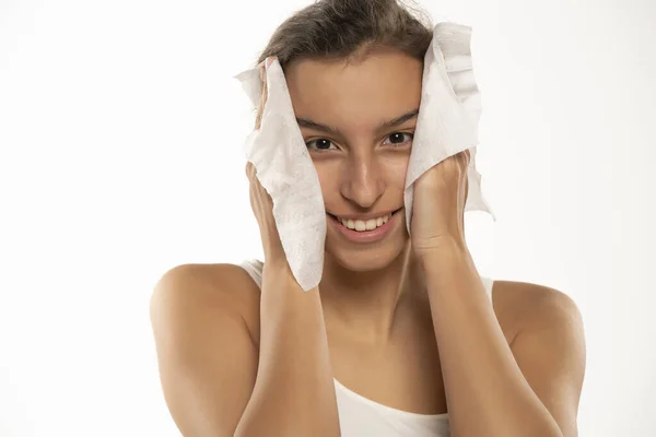 一个年轻的黑发女人用湿湿的湿巾擦拭她的脸的画像 女孩正在去除在白色工作室背景下分离的面部组织的化妆品 美容美发概念 — 图库照片