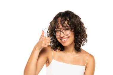 Gözlüklü, makyajsız, beyaz stüdyo arka planında baş parmak gösteren güzel Hintli genç bir kadının portresi.