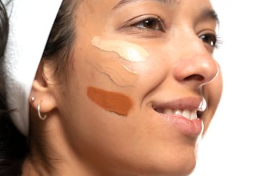 Beyaz stüdyo arka planında farklı tonlarda sıvı temeli olan koyu tenli bir kadının yüzü.