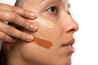 Beyaz stüdyo arka planında farklı tonlarda sıvı temeli olan koyu tenli bir kadının yüzü.