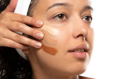 Beyaz stüdyo arka planında farklı tonlarda sıvı temeli olan koyu tenli bir kadının yüzü.