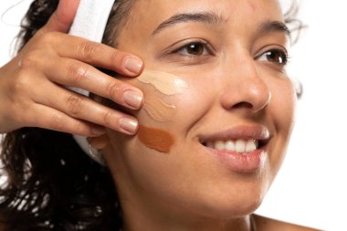 Beyaz stüdyo arka planında farklı tonlarda sıvı temeli olan koyu tenli bir kadının yüzü.