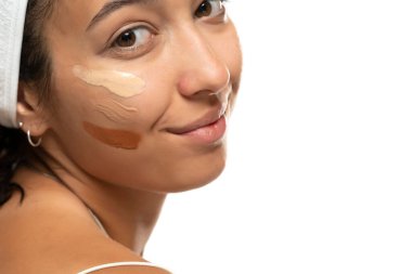 Beyaz stüdyo arka planında farklı tonlarda sıvı temeli olan koyu tenli bir kadının yüzü.