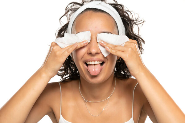 Portrait of a young funny brunette woman cleaning her face with wet wipes. Girl is removing make-up with facial tissues isolated on white studio background. Beauty skin care concept.