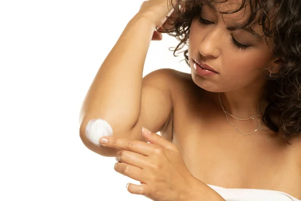 Head shot of a exotic woman takes care of her elbows using cosmetic cream on a white studio background