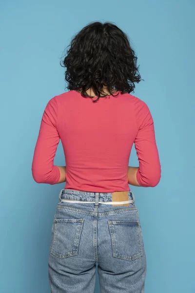 青いスタジオの背景にジーンズとピンクのブラウスの女性のバックビュー — ストック写真