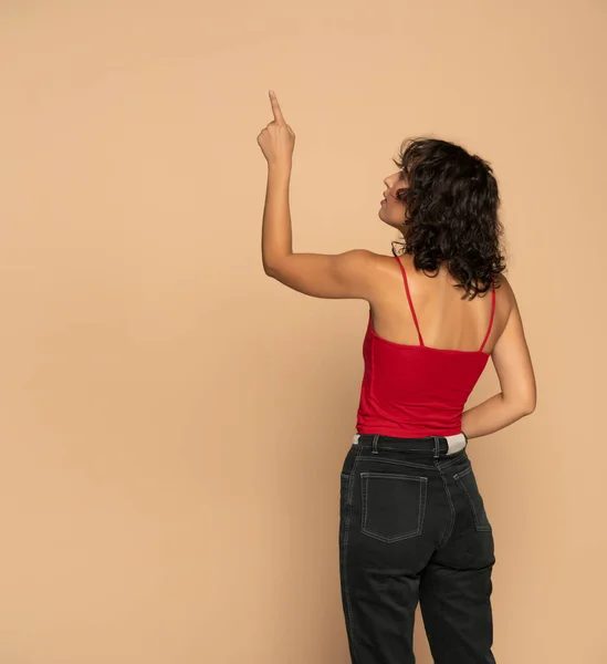 ベージュスタジオの背景に何かを指す若いダークスキンジードの女性 — ストック写真