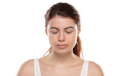 Makyajsız, uzun saçlı, beyaz bir stüdyoda gözleri kapalı genç bir kızıl kadın.