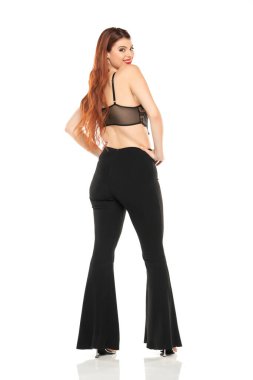 Moda tarzı stüdyo portresi. Güzel bir genç kadının. Siyah geniş paçalı pantolon ve siyah dantel sütyen. Beyaz stüdyo arka planına karşı duran ve poz veren model