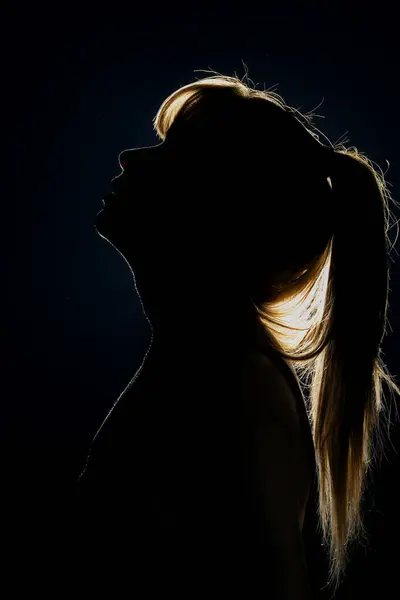 Silhouette of woman\'s head with ponytail, back light.