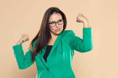Yeşil takım elbiseli iş kadını bej renkli stüdyo arka planında pazılarını gösteriyor.
