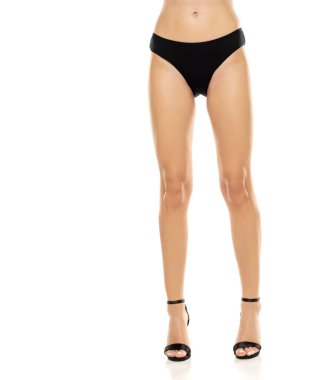 Yüksek topuklu ayakkabılar ve siyah külotla beyaz stüdyo arka planında kendine güvenen kadın bacaklarının zerafeti sergileniyor.