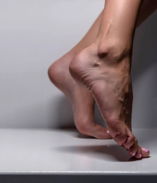 Closeup shot of healthy beautiful female feet. Visible veins. Side view of human foot on grey studio background
