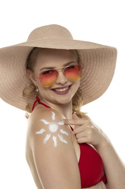 Kırmızı sutyenli güzel, gülümseyen sarışın kadın. Beyaz stüdyo arka planında, omzunda gülümseme şeklinde kozmetik ürünler var..