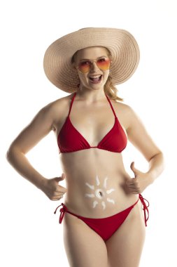 Kırmızı bikinili güzel, gülümseyen sarışın kadın. Beyaz stüdyo arka planında, göbeğinde güneş şeklinde kozmetik ürünler var..