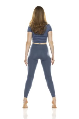 Tüm vücut, dikiz aynası spor giyimli genç kadın beyaz stüdyo arka planında poz veriyor.