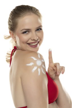 Kırmızı sutyenli güzel, gülümseyen sarışın kadın. Beyaz stüdyo arka planında, omzunda gülümseme şeklinde kozmetik ürünler var..