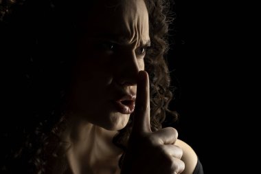 Yüzü gölgede, siyah stüdyo arka planında parmaklarını dudaklarında tutan sinirli, tanınmış bir kadının silueti.