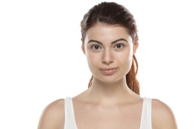 Makyajsız, uzun kızıl saçlı, beyaz bir stüdyo arkasında genç bir kadın.