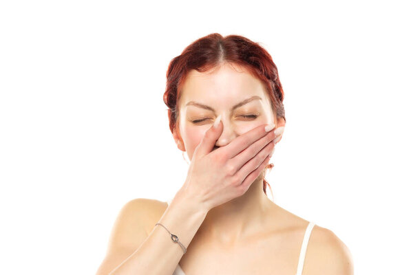 Portrait of a young smiling woman without makeup covering her mouth with her palm on a white studio background