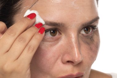 Genç bir kadın beyaz stüdyo arka planındaki makyajı kaldırıyor.