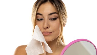 Çekici genç bir kadın beyaz stüdyo arka planında ıslak mendille yüzünü temizliyor.