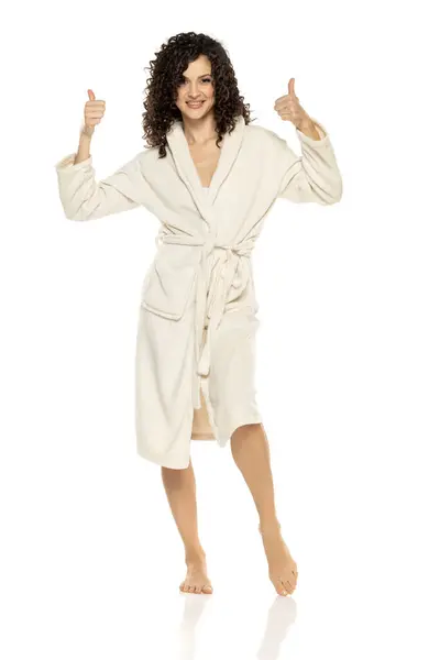 年轻快乐的女人穿着浴衣 在白色的工作室背景上竖起大拇指 免版税图库照片
