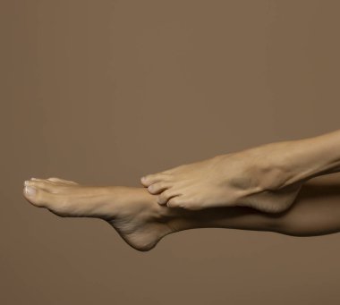 Bej renkli stüdyo arka planında poz veren kadın ayaklarının yan görüntüsü.