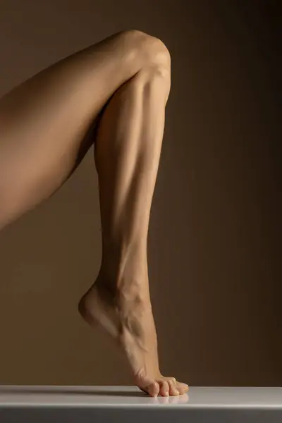 closeup, side view of female foot and leg posing on beige studio background