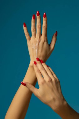 Mavi stüdyo arka planına losyon kremi süren bir kadın.