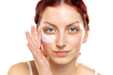 Genç kızıl saçlı kadın beyaz stüdyo arka planına yüz estetiği uyguluyor.