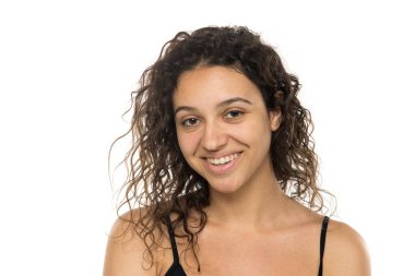 Beyaz stüdyo arka planında, kıvırcık saçlı ve makyajsız gülümseyen genç bir kadının portresi.