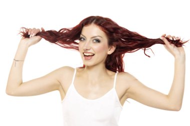 Tişörtlü mutlu bir kızıl kadın uzun saçlarını beyaz stüdyo arka planında gösteriyor.