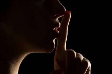 Yüzü gölgede, siyah bir stüdyoda dudaklarını tutan kimliği belirsiz bir kadının profili.