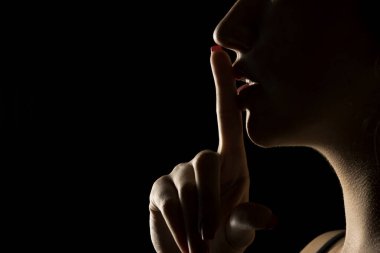 Yüzü gölgede, siyah bir stüdyoda dudaklarını tutan kimliği belirsiz bir kadının profili.