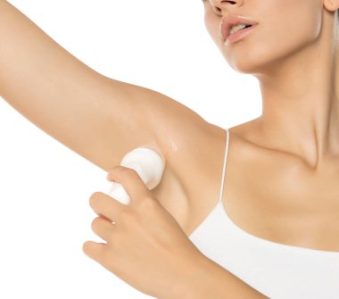 Beyaz bir stüdyo arka planında kolunun altına deodorant sıkan bir kadın.