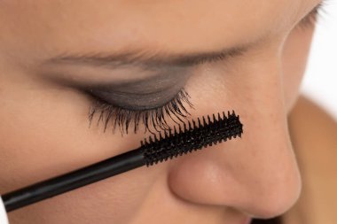 Güzel bir kadın beyaz stüdyo arka planına rimel sürüyor.