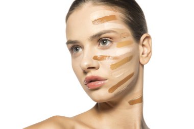 Yüzünde farklı bir sıvı fondöten tonuyla poz veren güzel genç kadın.