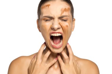 Güzel, kızgın ve çığlık atan bir kadın yüzüne farklı tonlarda sıvı fondöten sürüyor.