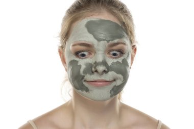 Yüzünde yarı kurumuş yeşil çamur maskesiyle poz veren komik bir genç kadın. Cilt bakımı ve tedavisi, spa, doğal güzellik ve kozmetoloji konsepti.