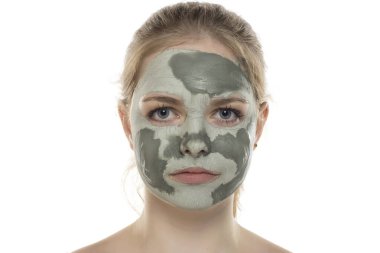 Yüzünde yarı kurumuş yeşil çamur maskesiyle poz veren genç bir kadın. Cilt bakımı ve tedavisi, spa, doğal güzellik ve kozmetoloji konsepti.