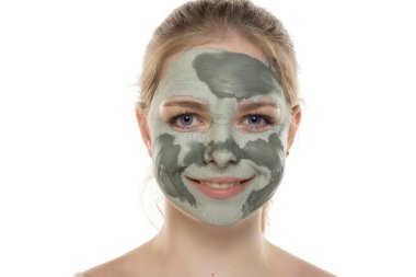 Yüzünde yarı kurumuş yeşil çamur maskesiyle poz veren genç bir kadın. Cilt bakımı ve tedavisi, spa, doğal güzellik ve kozmetoloji konsepti.