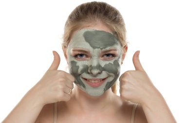 Yüzünde yarı kurumuş yeşil çamur maskesiyle poz veren genç bir kadın. Cilt bakımı ve tedavisi, spa, doğal güzellik ve kozmetoloji konsepti.