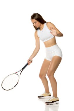 Beyaz stüdyoda tenis raketiyle poz veren genç ve güzel bir kadın.