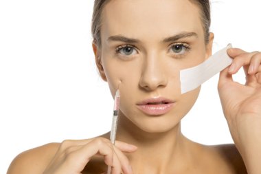 Genç ve güzel bir kadın yüzüne bir şırınga enjekte eder ve deriyi yapıştırıcı bant ile sıkar.