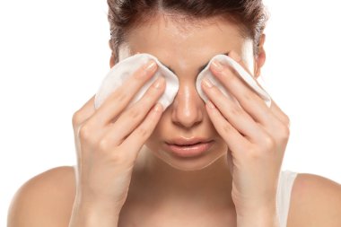 Güzel kızıl saçlı kadın beyaz stüdyo arka planında pamuklu çubukla yüzünü temizliyor. 