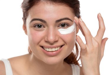 Güzel, gülümseyen, kızıl saçlı bir kadın beyaz bir stüdyo arka planına makyaj kremi sürüyor.